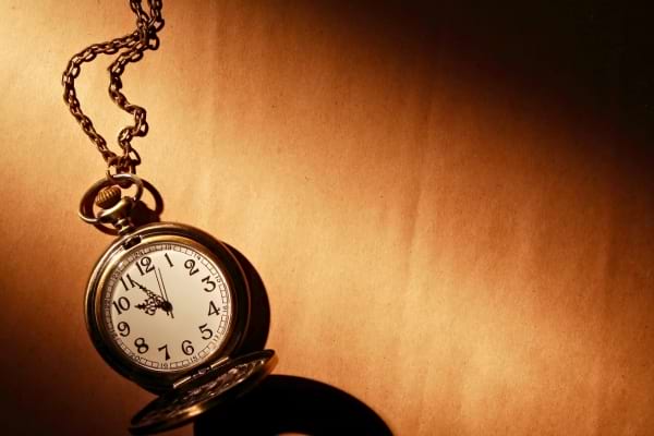 Une montre à gousset ancienne repose sur un fond éclairé en clair-obscur.