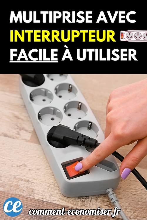 Une main appuyant sur l’interrupteur rouge d’une multiprise posée sur un sol en bois.