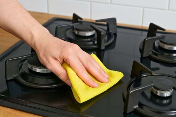 Main terminant le nettoyage d’une plaque avec chiffon jaune.