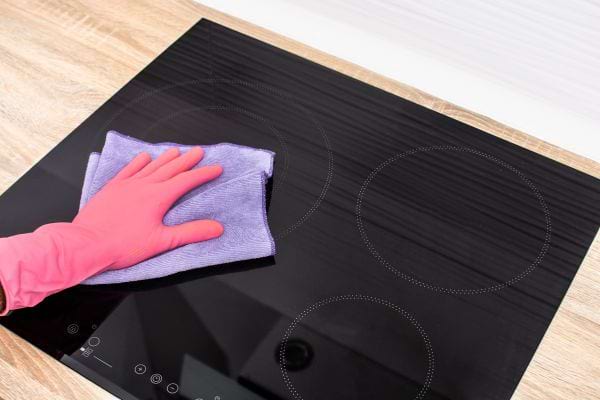 Main gantée nettoyant une plaque de cuisson noire avec un chiffon.