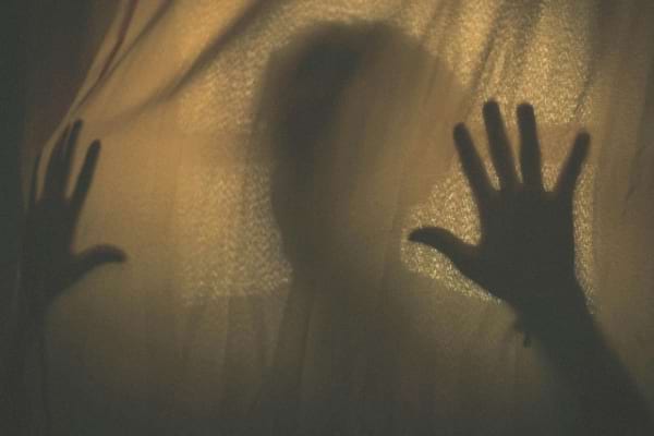 Une silhouette floue et des mains sont projetées en ombre derrière un tissu.   
