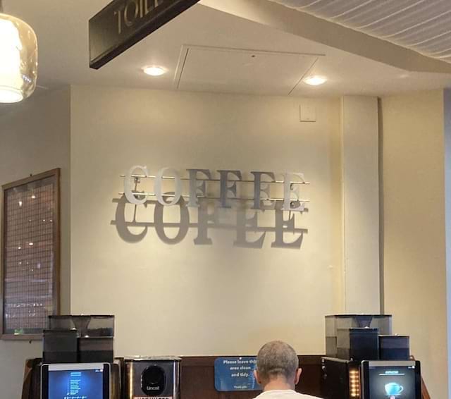 Panneau “COFFEE” projetant une ombre décalée sur le mur.