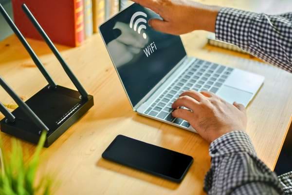 Ordinateur portable affichant connexion Wi-Fi avec routeur et smartphone sur bureau.