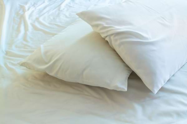 Deux oreillers blancs sont posés sur un lit parfaitement fait avec des draps blancs.