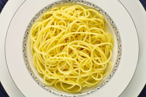 Une assiette blanche contient une portion de spaghetti cuits sans sauce, soigneusement dressés en spirale.