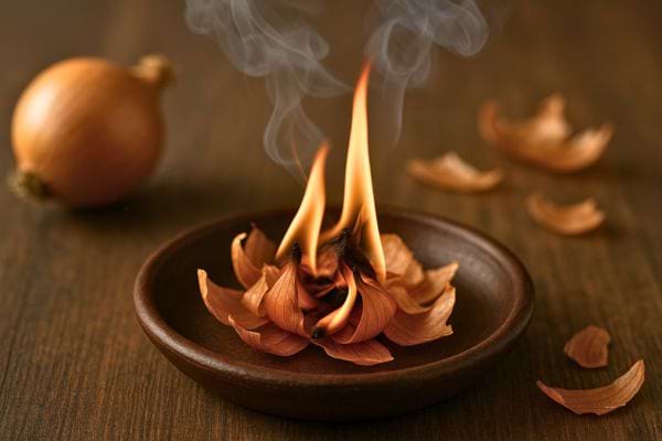 Des pelures d’oignon brûlent dans une coupelle en bois, dégageant de la fumée.