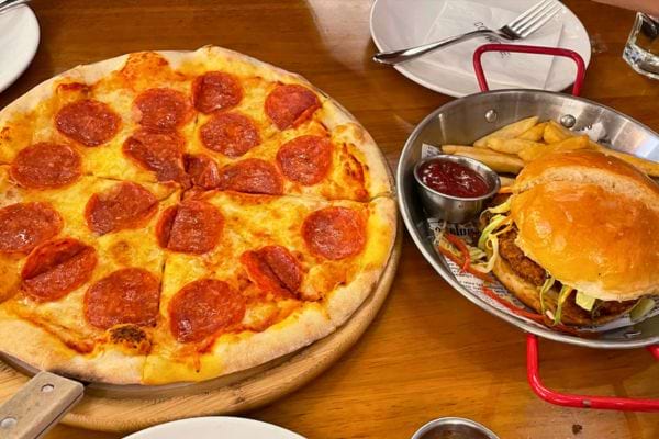 Une pizza au pepperoni et un burger avec frites sont posés sur la table.