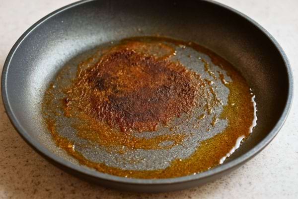 Une poêle noire avec des résidus brûlés et de la graisse.