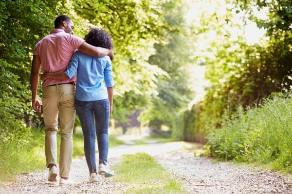 Un couple marche enlacé sur un chemin boisé, dos tourné, moment paisible en nature.