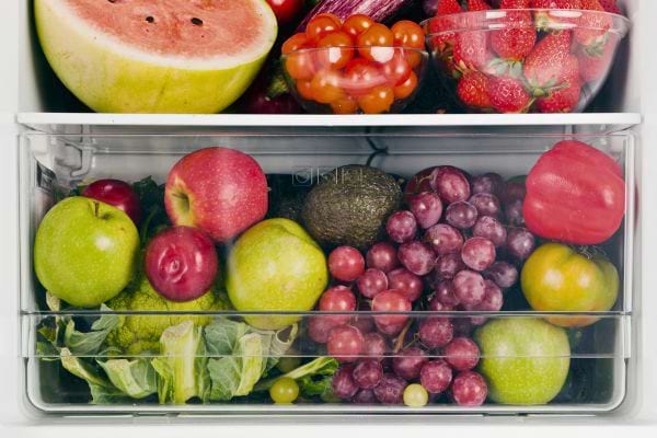 Un tiroir de réfrigérateur rempli de raisins rouges, pommes, tomates et autres fruits.