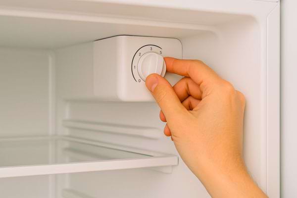 Une main règle la température à l’intérieur d’un frigo vide.