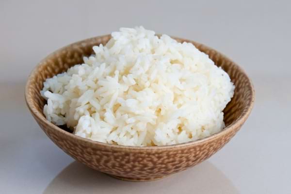Un bol marron est rempli de riz blanc bien cuit, aux grains légèrement collés les uns aux autres.