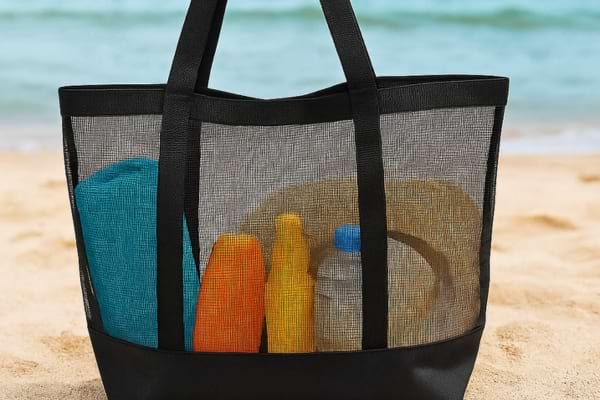 Un sac de plage en filet transparent contenant une serviette, des crèmes et une bouteille.