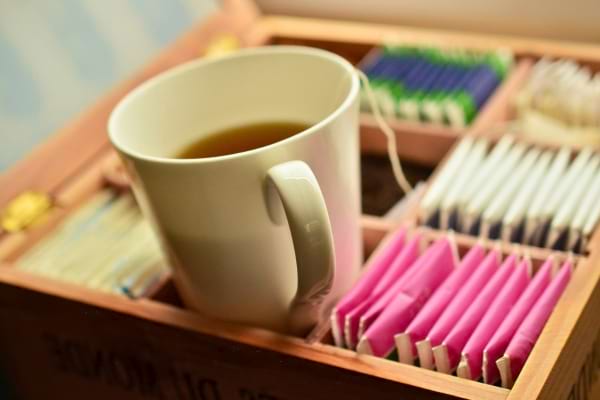 Une tasse de thé fumant est posée dans une boîte contenant des sachets de thé de différentes couleurs.