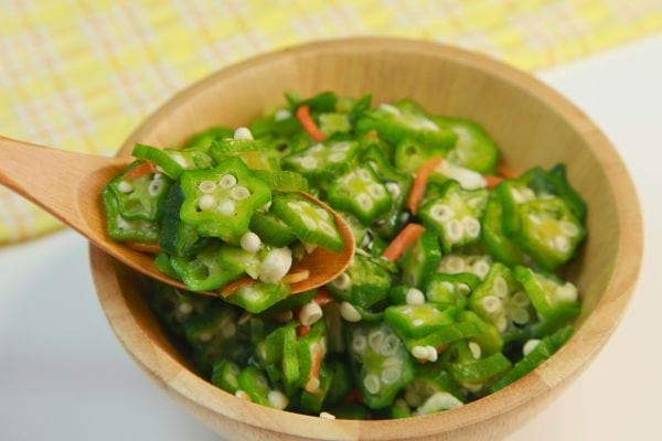 Une cuillère en bois sert des rondelles de gombo dans un bol.