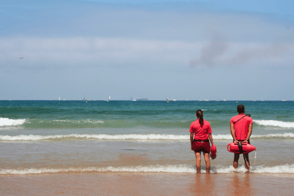 Deux sauveteurs en tenue rouge surveillent la mer depuis le rivage.