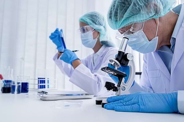 Deux scientifiques en blouse blanche analysent des échantillons au microscope.