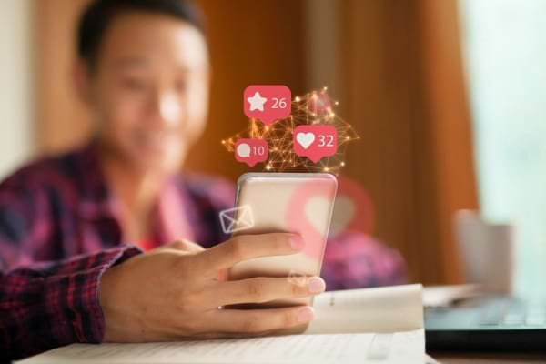 Un jeune regarde son téléphone avec des notifications de réseaux sociaux visibles à l’écran.
