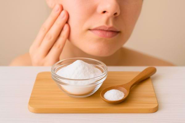 Une femme touche sa joue près d’un bol rempli de bicarbonate et d’une cuillère en bois.