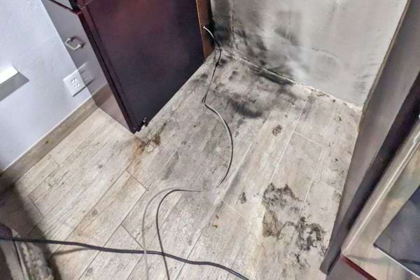 Un sol très sale taché d’humidité et de traces noires près d’un mur.