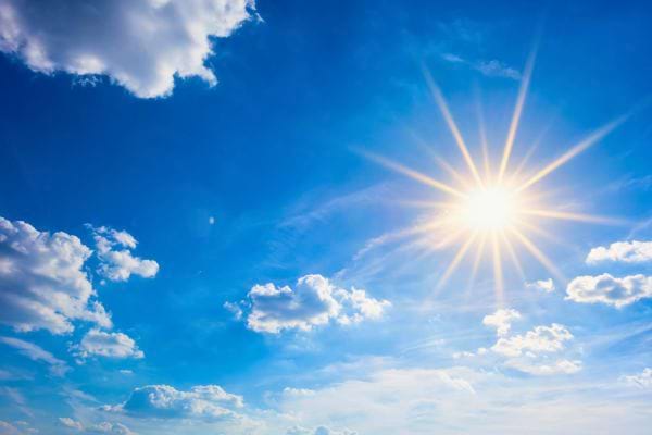 Le soleil brille intensément dans un ciel bleu avec quelques nuages.