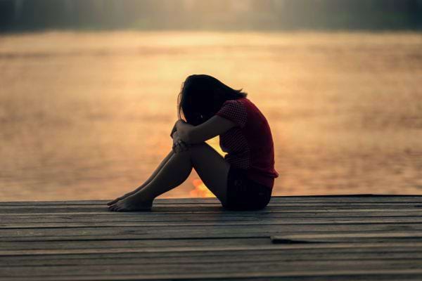 Une femme assise seule près de l’eau au coucher du soleil.