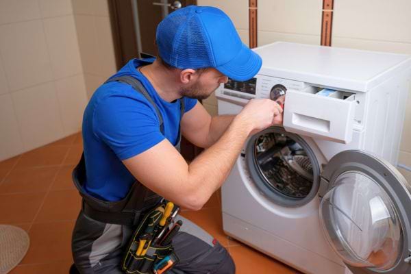 Un technicien en bleu répare une machine à laver ouverte.