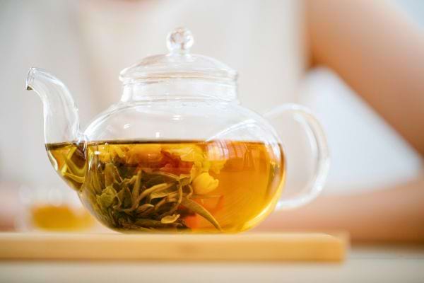 Théière en verre remplie d’infusion chaude avec des feuilles d’estragon visibles.