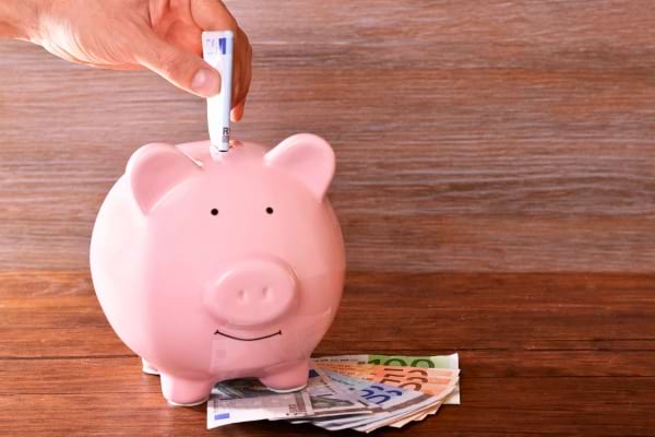 Main mettant un billet roulé dans une tirelire cochon rose.