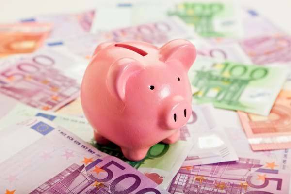 Une tirelire rose en forme de cochon est posée sur un tas de billets en euros.  