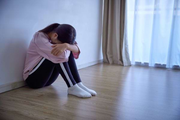 Une jeune fille assise contre un mur cache son visage.