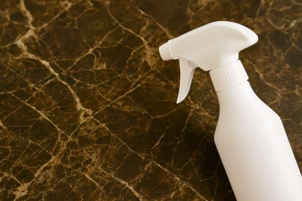 Un vaporisateur blanc est posé sur une surface en marbre foncé.