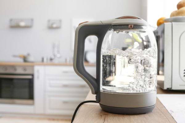 Bouilloire en verre sur un plan de travail, eau bouillante à l’intérieur.