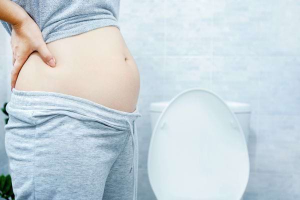 Une personne enceinte se tient le ventre douloureux devant des toilettes.