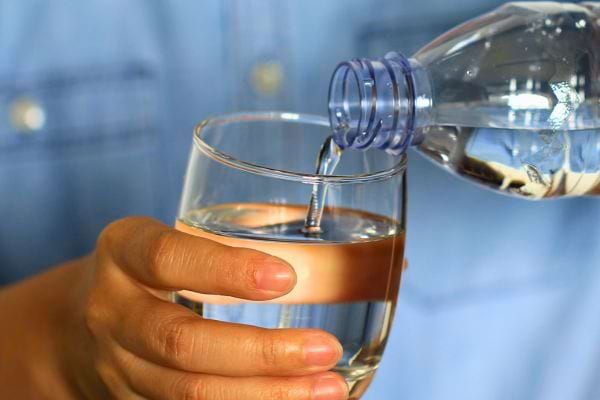 Un verre d’eau est versé d’une bouteille tenue à la main.