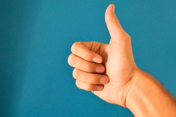 Une main fait un signe de pouce levé devant un fond bleu.