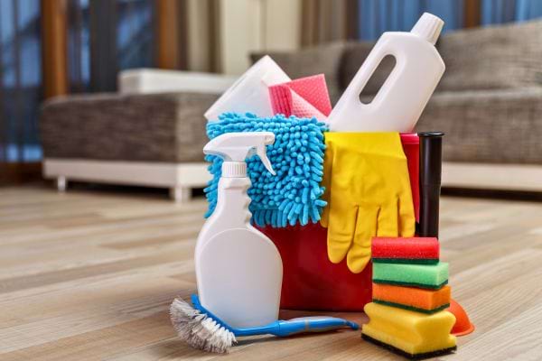 Un seau rouge contient des produits ménagers, gants, éponges et brosses de nettoyage.