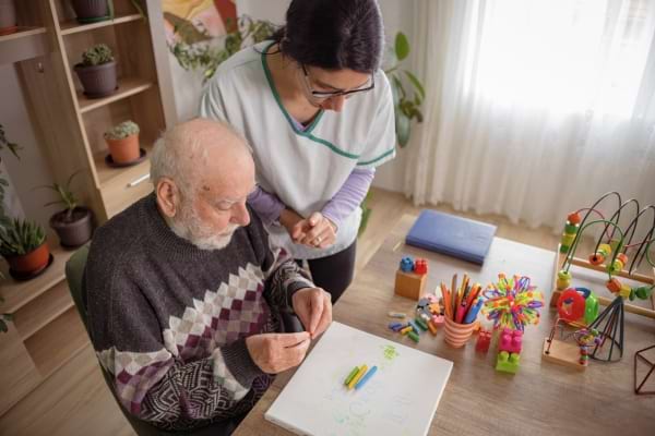 Un soignant aide un senior à réaliser une activité manuelle colorée.