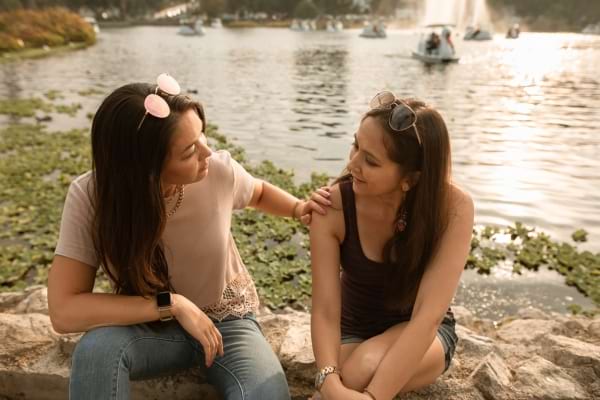 Deux amies discutent assises près d’un lac, dans une ambiance apaisée.