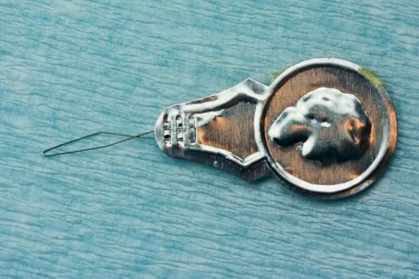 Un passe-fil argenté ancien avec une tête gravée en relief.