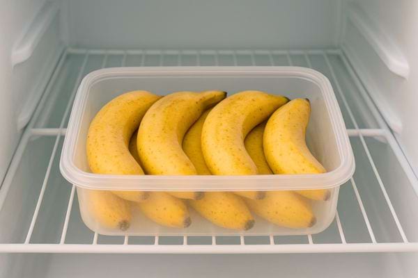 Des bananes jaunes entières rangées dans une boîte plastique placée au réfrigérateur.
