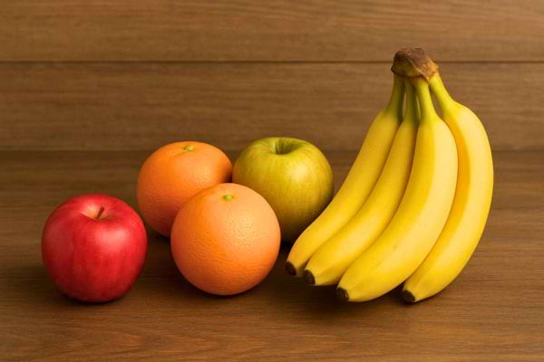 Des bananes posées sur une table avec pommes et agrumes à côté.