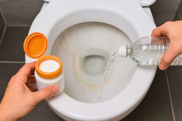 Du bicarbonate et du vinaigre sont versés dans la cuvette des toilettes.