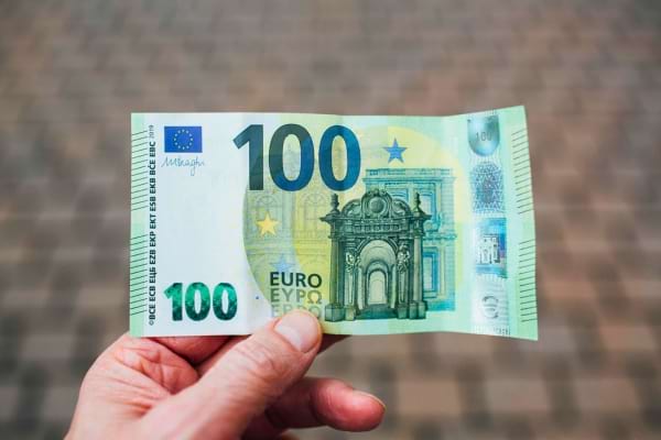 Un billet vert de 100 euros tenu par une main.