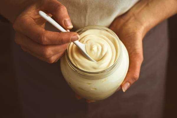 Une personne tient un bocal rempli de mayonnaise crémeuse avec une cuillère.