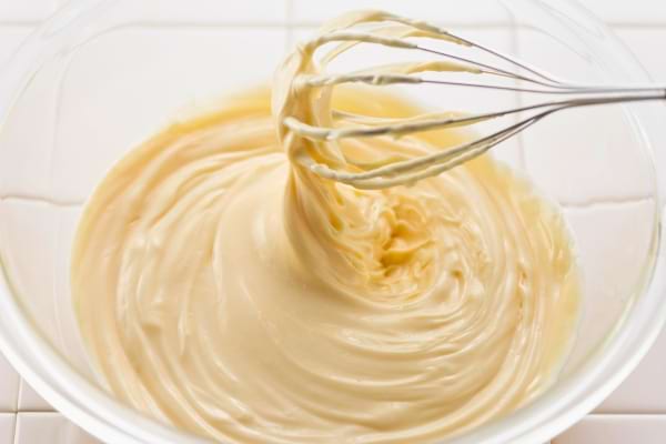 Un fouet mélange une mayonnaise crémeuse dans un grand bol transparent.