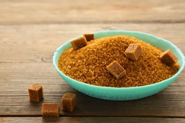 Un bol turquoise rempli de sucre roux en grains et de morceaux en cubes.