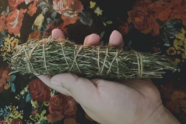 Une main tient une botte de romarin séché attachée avec de la ficelle.