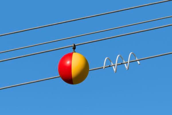 Une boule rouge et jaune est fixée à un câble électrique dans le ciel bleu.