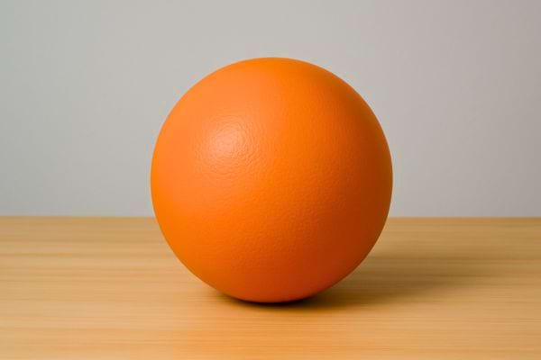 Une boule orange bien ronde repose seule sur une table en bois clair.